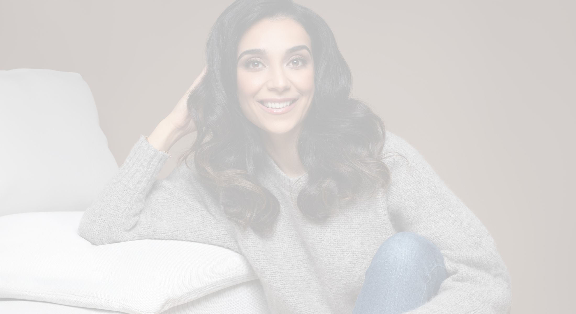 Smiling woman in cozy sweater on a couch.