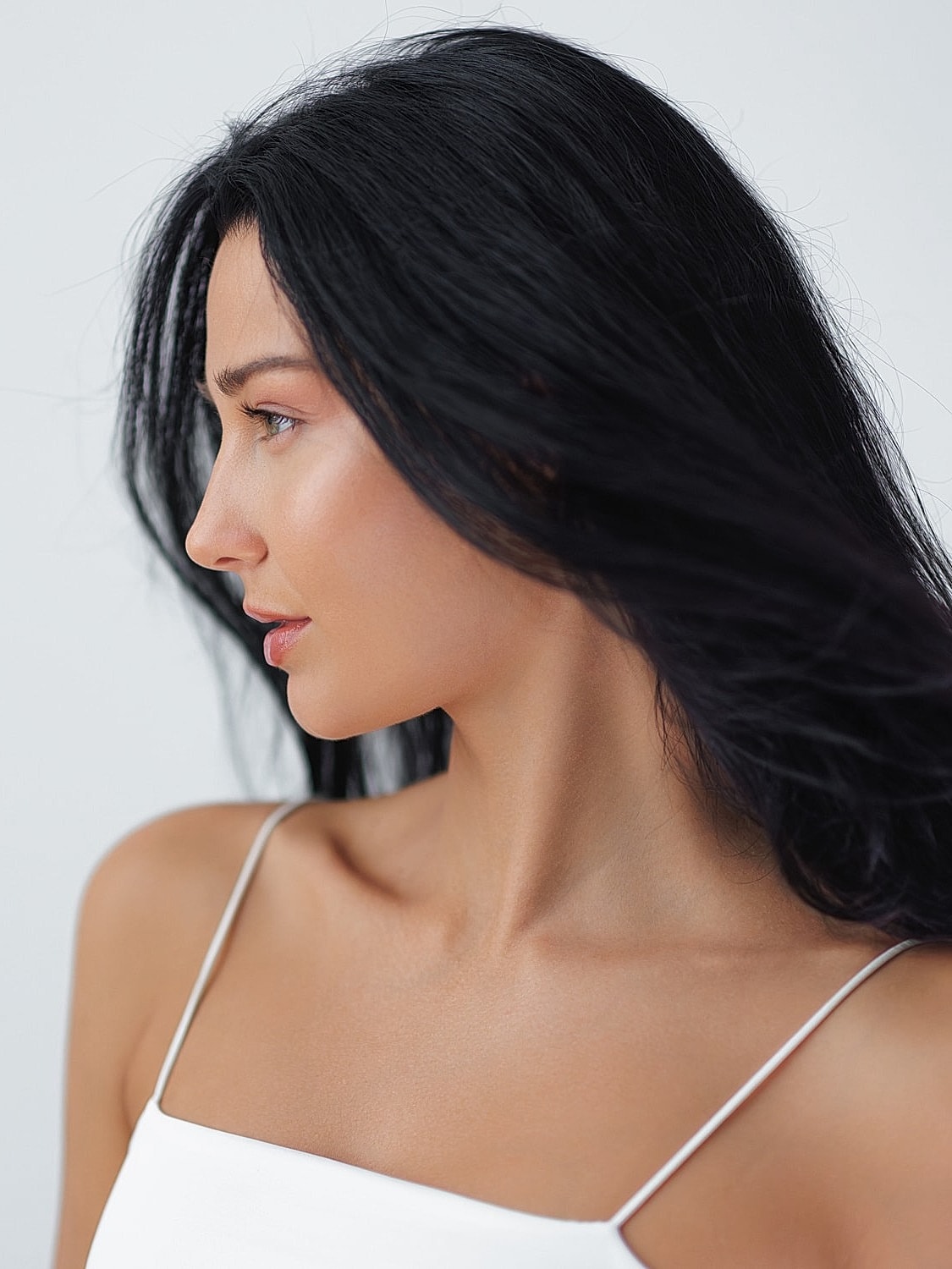 Woman in white top, profile against light background.
