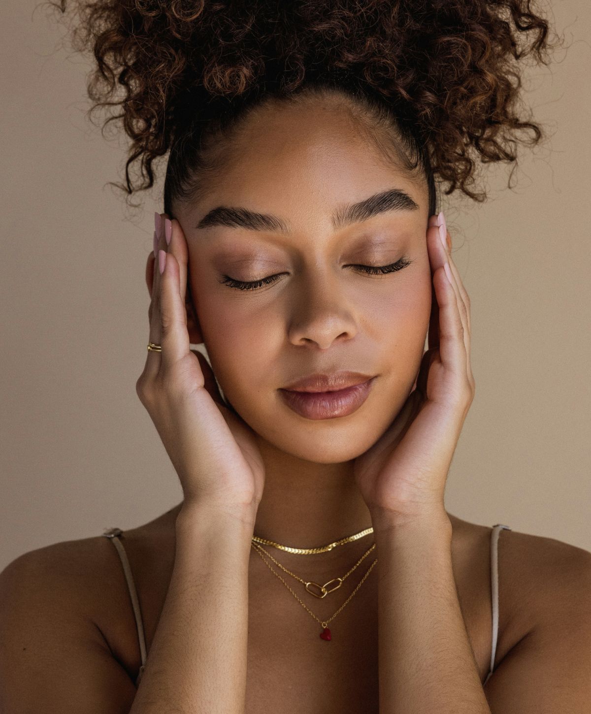 Woman with curly hair touching her face softly.