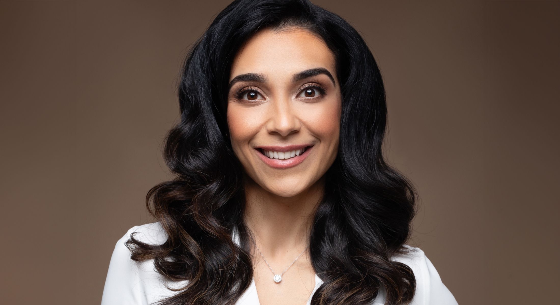 Smiling woman with long dark hair and necklace.