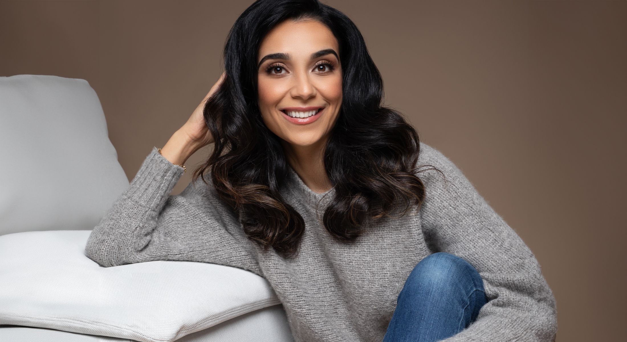 Smiling woman in sweater sitting on couch.