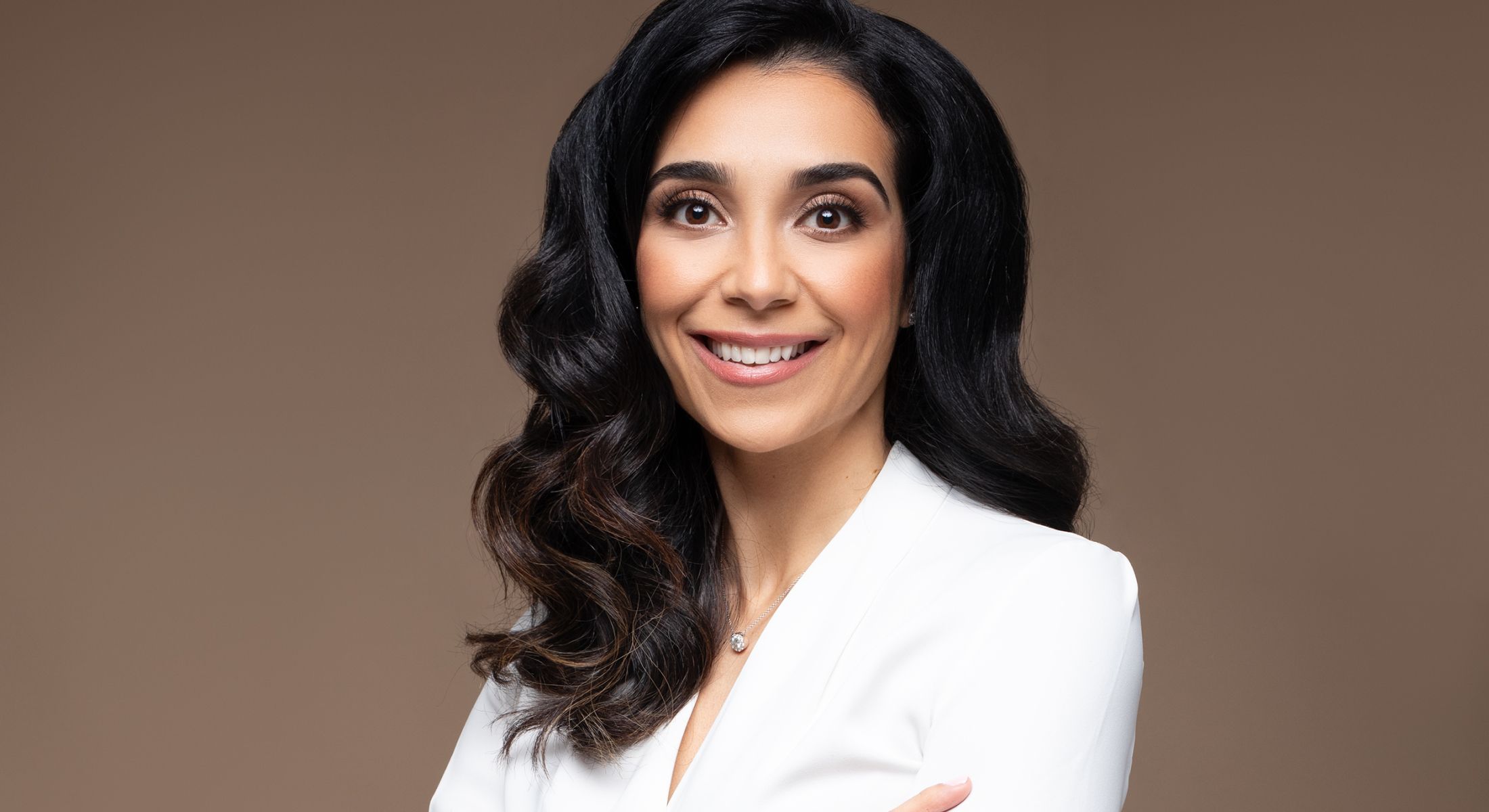 Smiling woman in a white blazer on brown background.