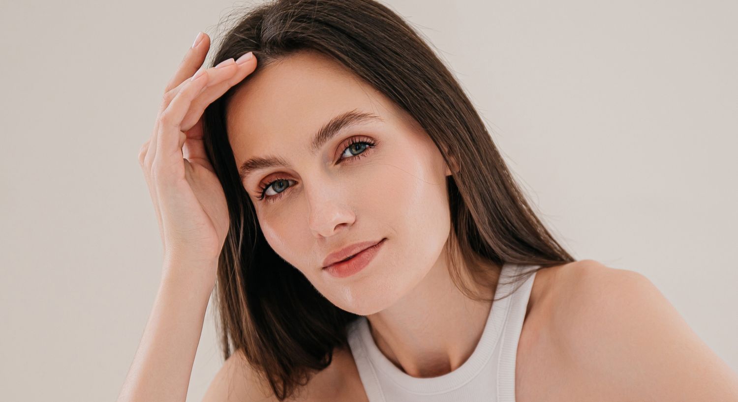 Woman touching her hair, soft smile, neutral background.
